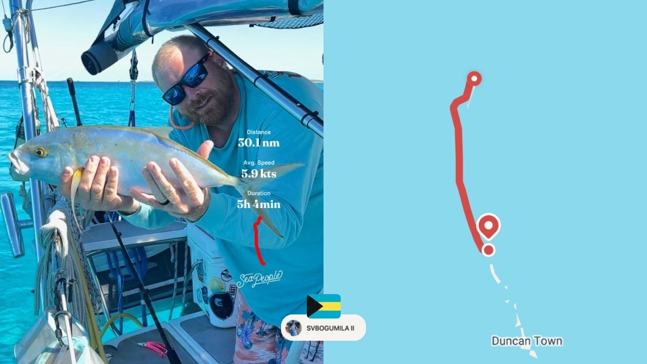 A man on a sailboat holds up a fish he caught in Duncan Town
