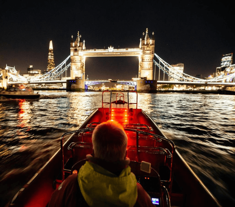 Thames Rockets Nights Speedboat Experience: The sleek red Thames Rocket RIB nose points at the Tower Bridge which is alight against the dark night sky.