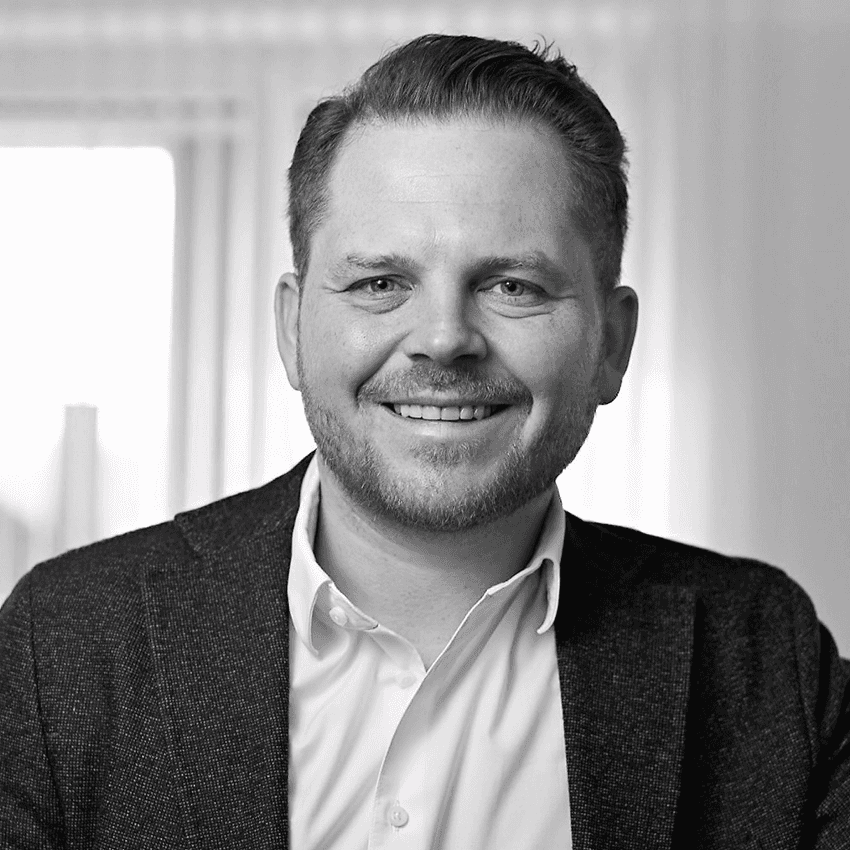 Porträt eines lächelnden Mannes mit Bart und Blazer. Er schaut freundlich in die Kamera.