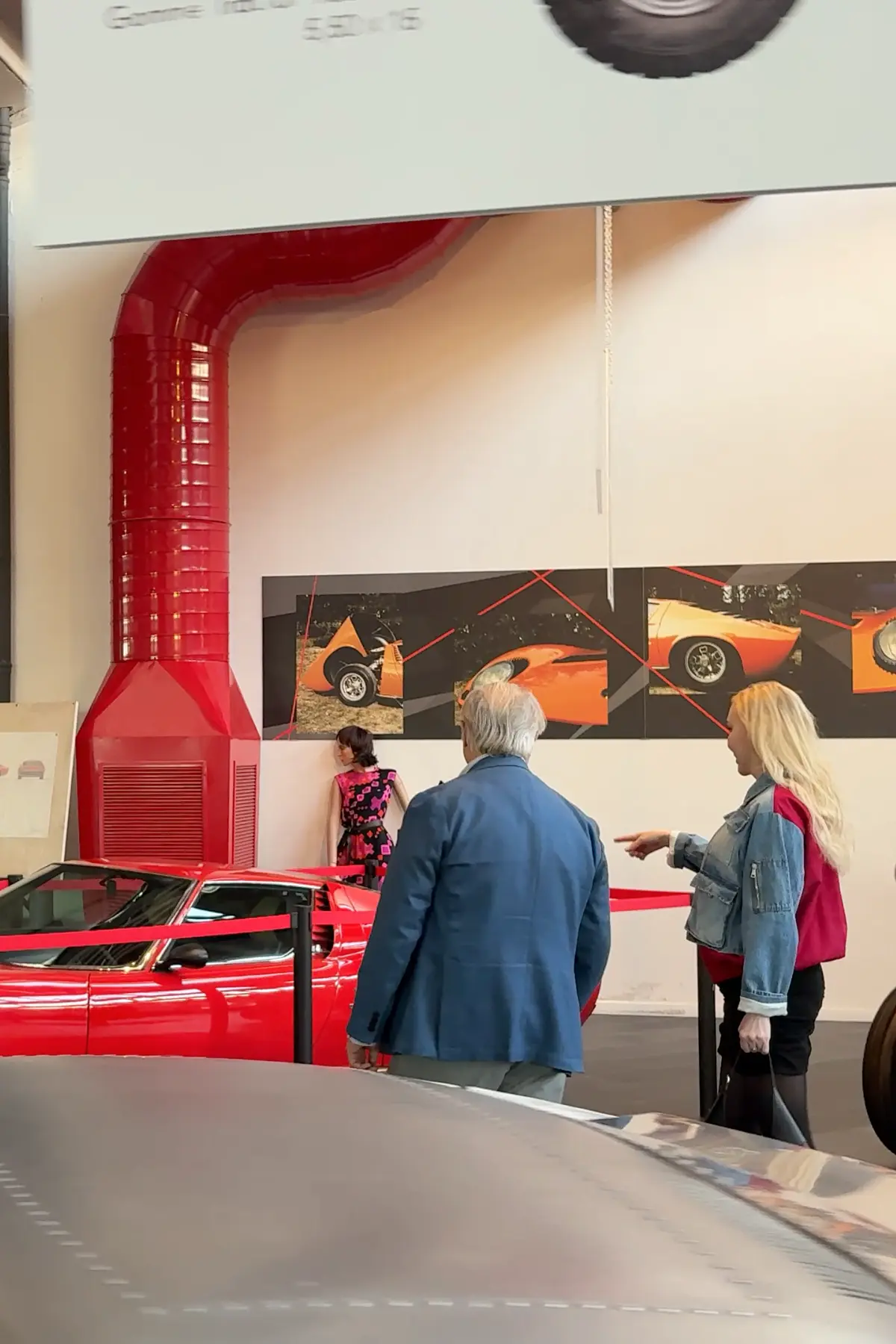 Elena pointing at a red Lamborghini while speaking with Tonino Lamborghini inside the museum