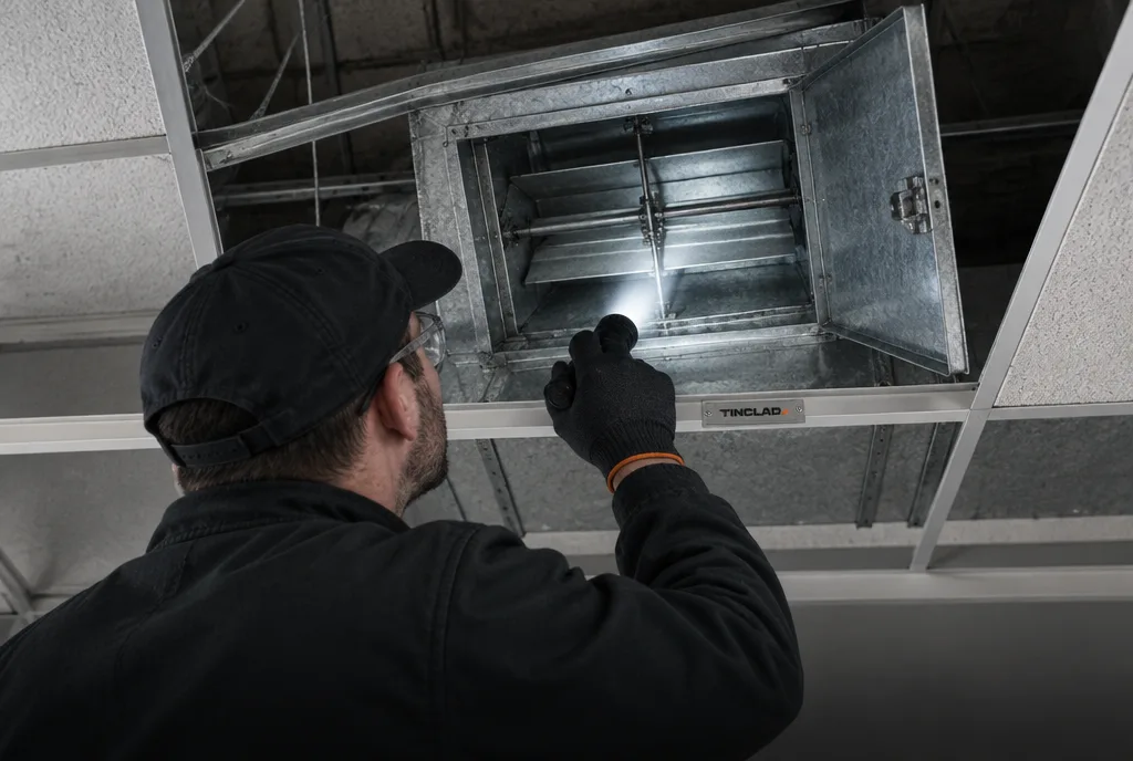 Tinclad technician inspecting a fire damper above a ceiling.