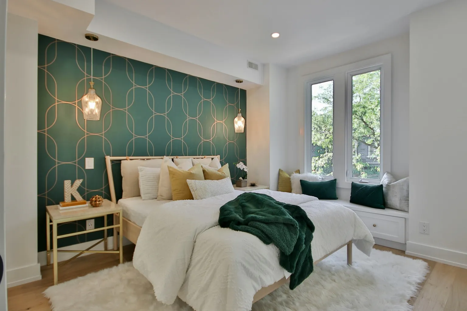 Camera da letto accogliente con parete verde decorata, letto matrimoniale con cuscini bianchi e verdi, e ampie finestre