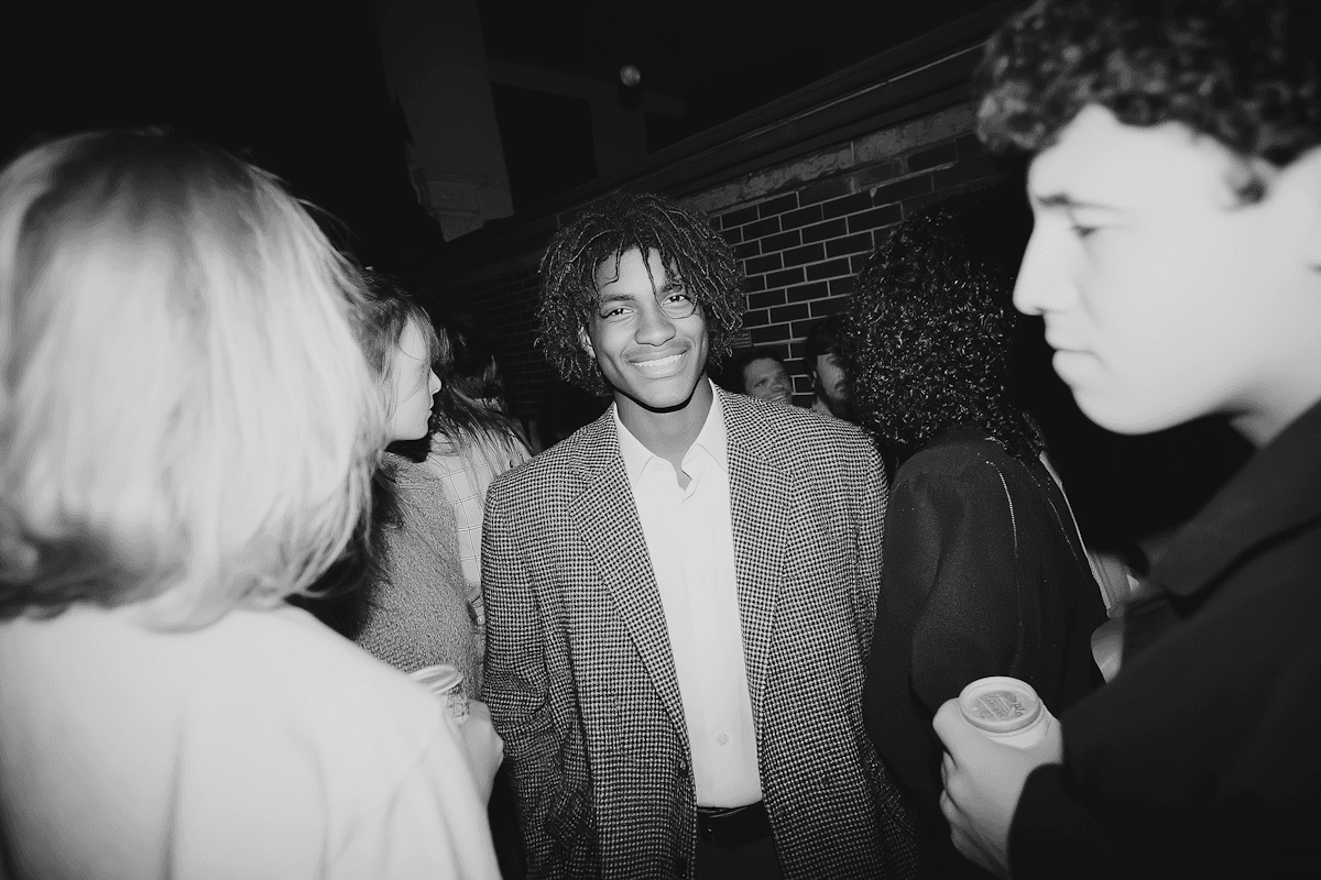 Black-and-white party photo of a smiling man in a check blazer among a crowd.