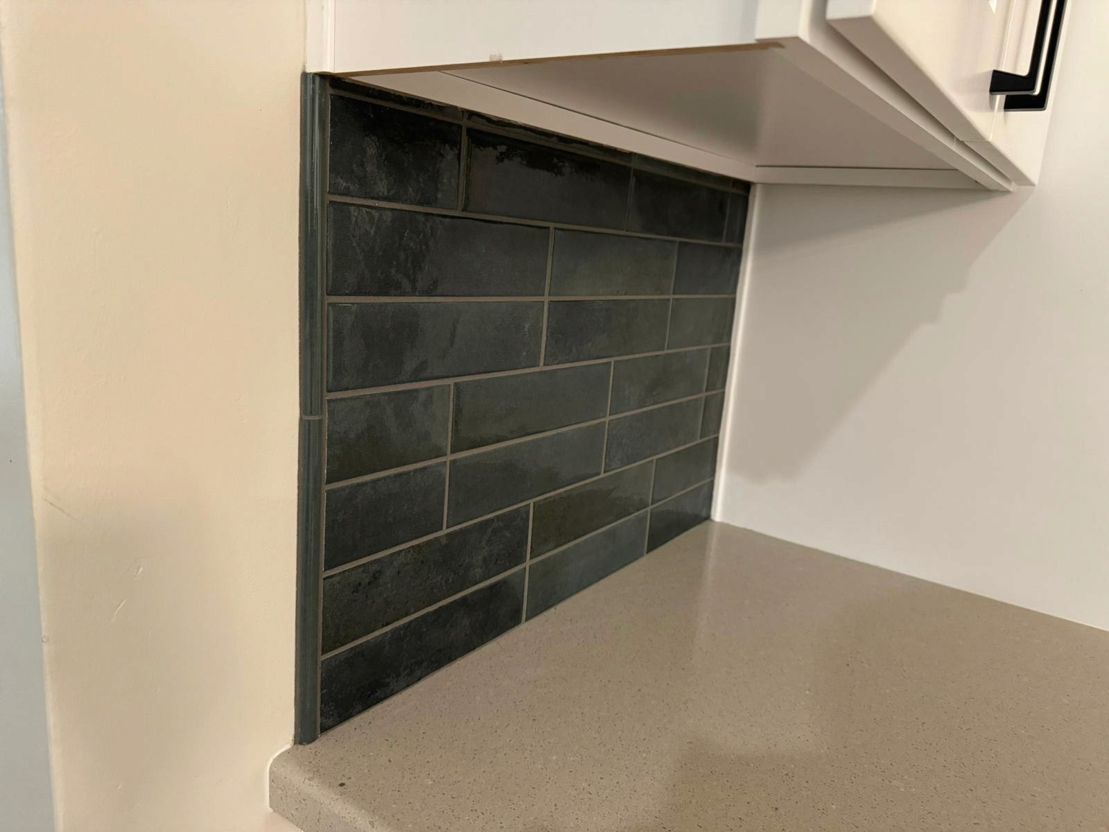 Modern kitchen with a dark subway tile backsplash and white cabinetry above a beige countertop.