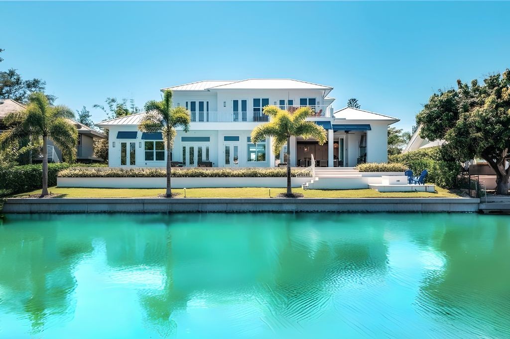 a white and blue property on the water with palm trees lining the sea wall