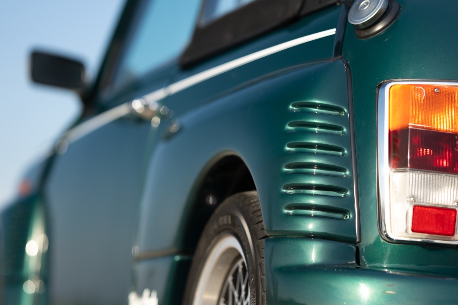 Close-up of a green vintage car's rear fender and wheel, showcasing its classic design and details.