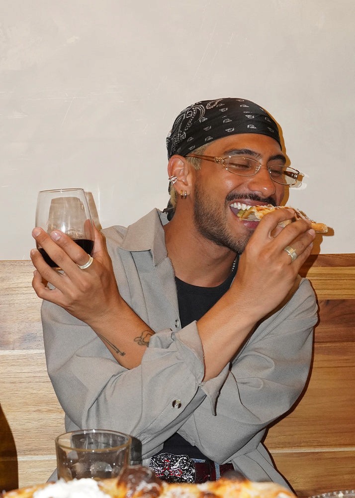 Man eating pizza and holding a glass of red wine indoors. With silver rings.