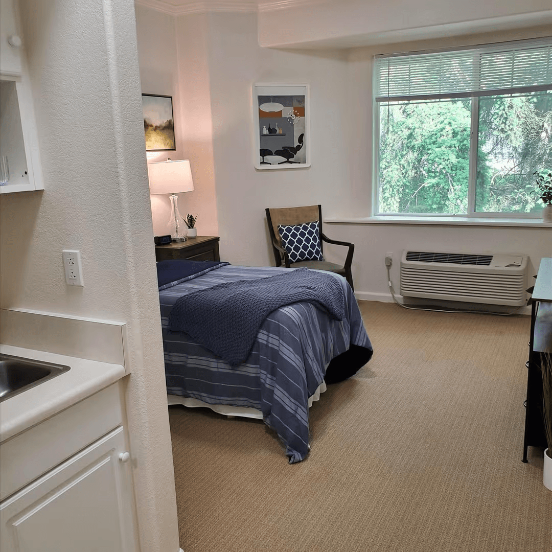 Private memory care bedroom with bed, accessible bathroom, and in-room sink designed for comfort and safety.