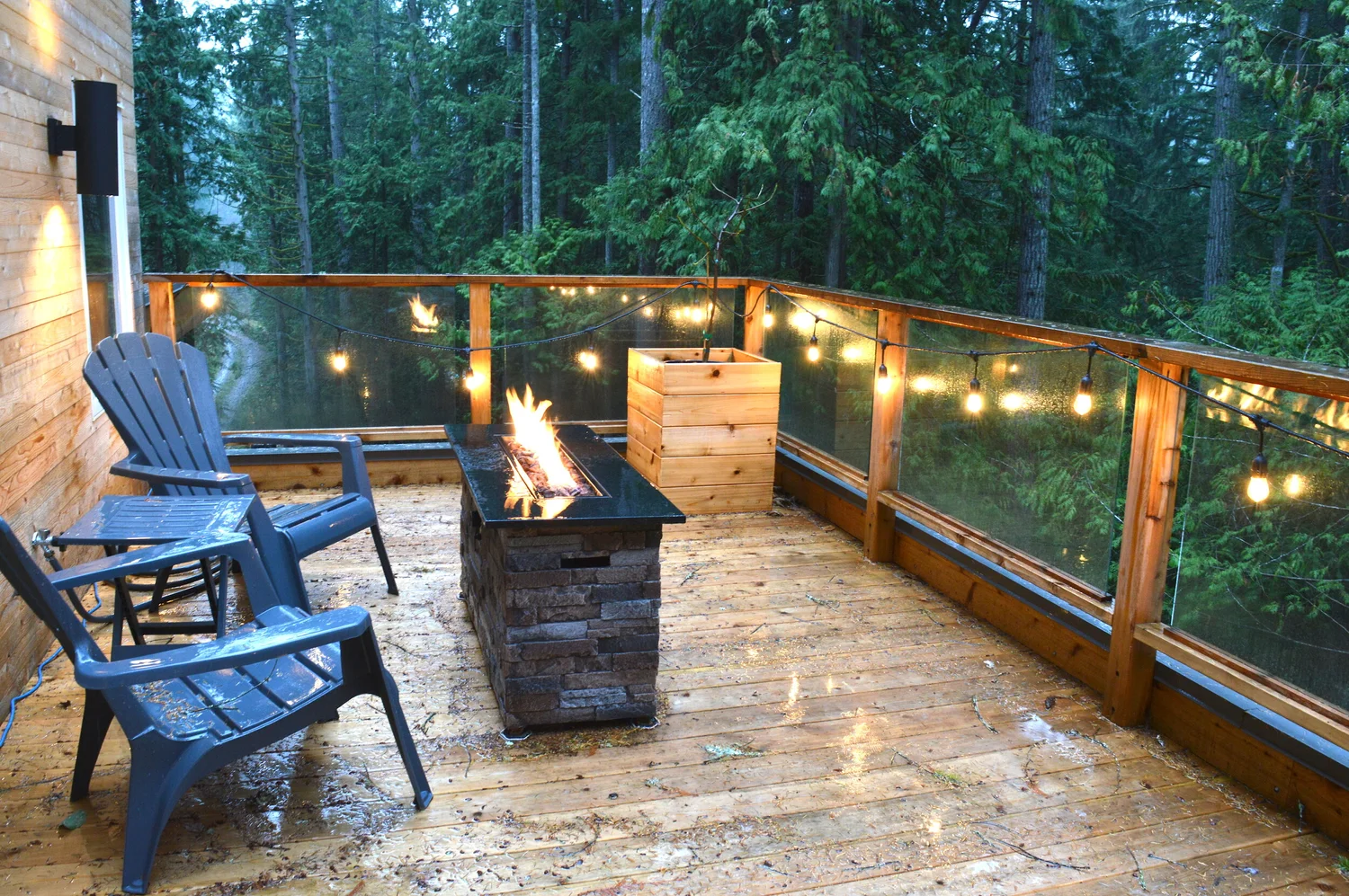 Modern two-story home with large glass windows, warmly lit interiors, and a balcony. Surrounded by trees and a manicured lawn at dusk. Cozy ambiance.