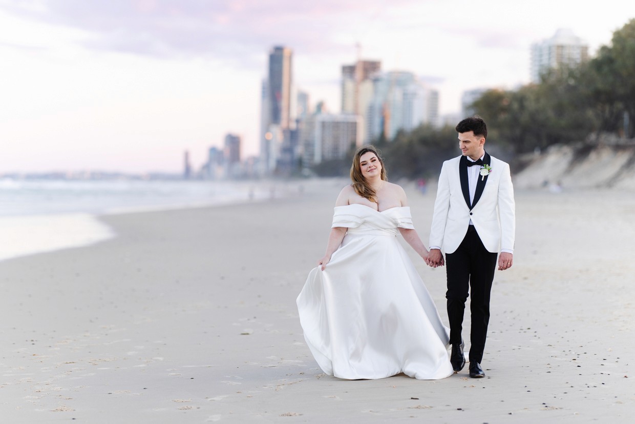 Bride and groom holding hands walking down the beach