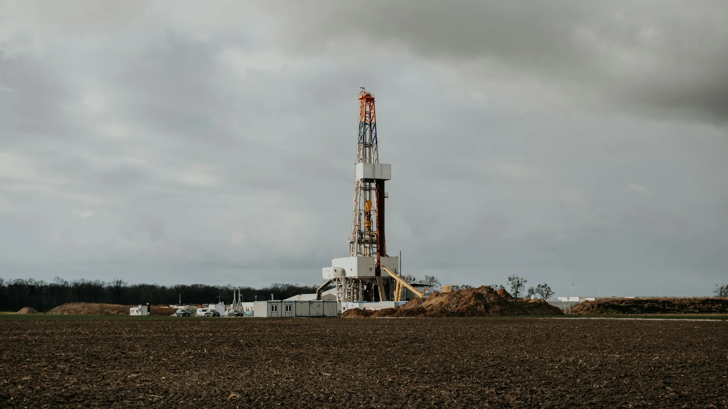 A land drilling rig standing in a plowed field under a cloudy sky