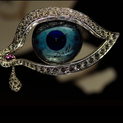סיכת תכשיט בצורת עין, הכוללת פני שעון בגוון כחול עם השם "דאלי" ודמעה יחידה.
