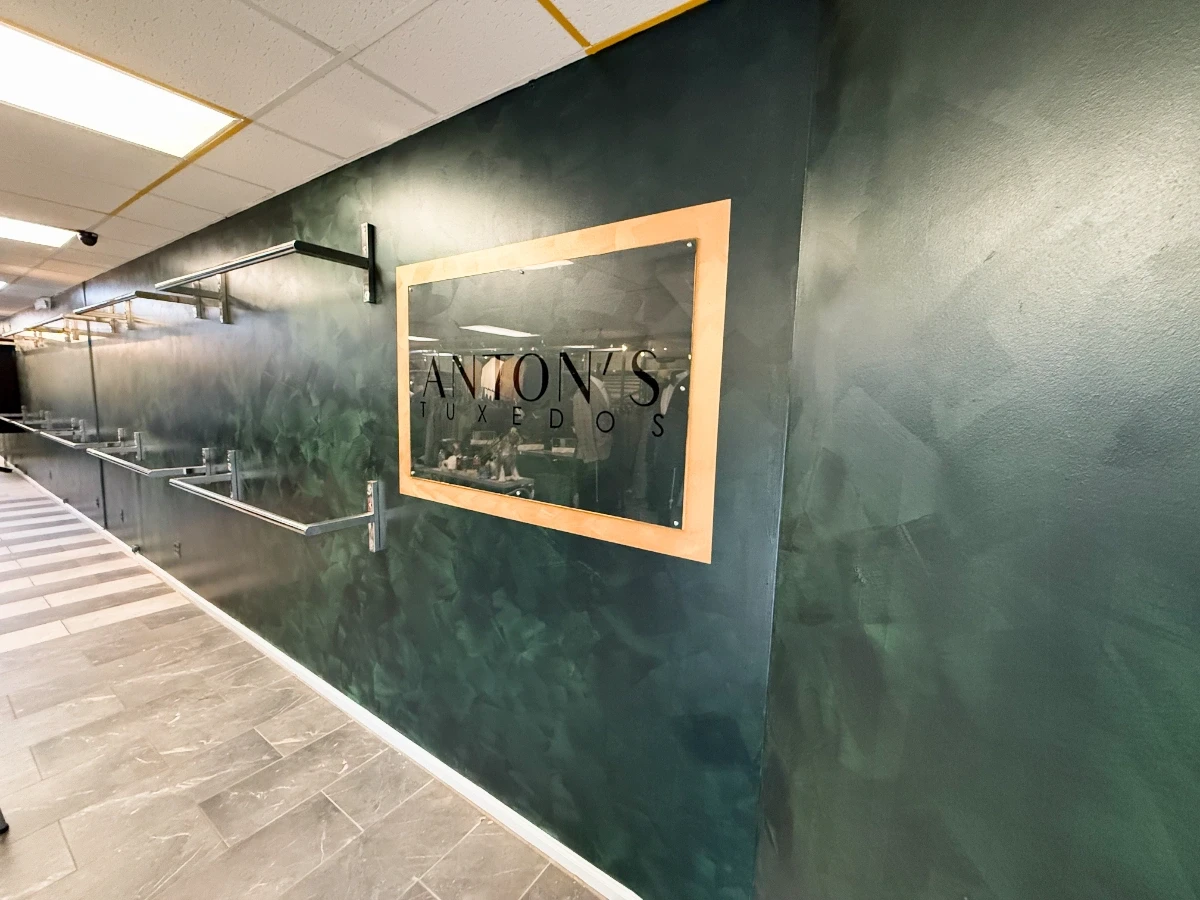 After renovation—Anton’s Tuxedos showroom wall featuring a deep green textured finish and framed glass logo display.
