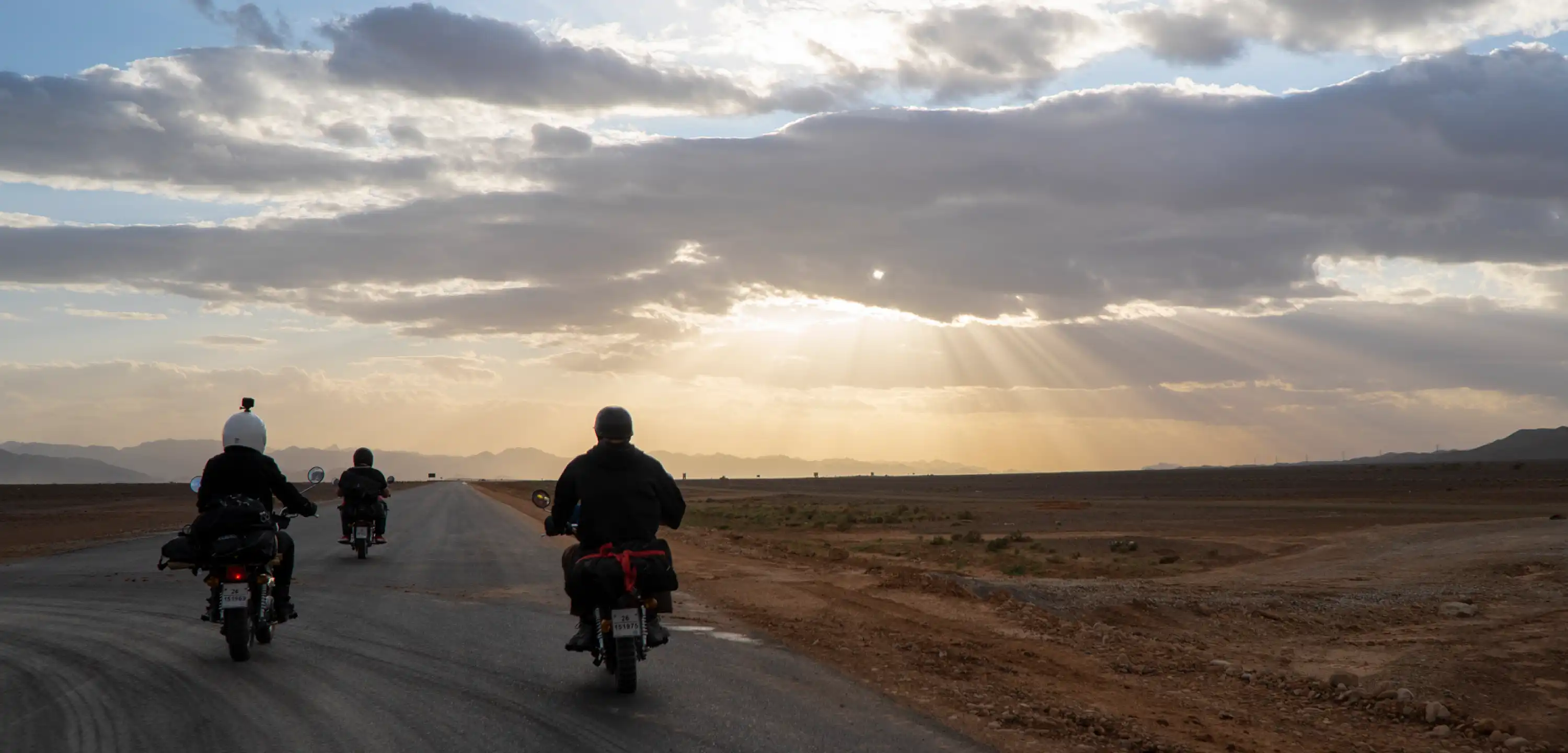 Three motorcycle riders riding down the road at sunset, one with an action camera on their helmet.