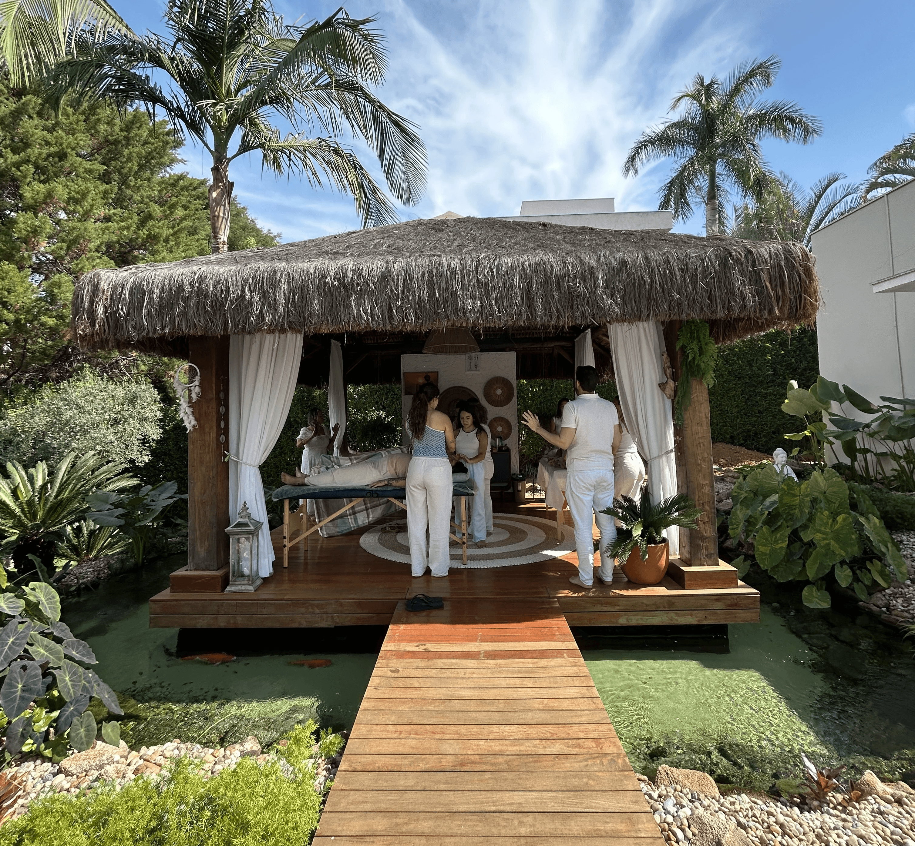 A circle of people sitting cross-legged, meditating with hands in a prayer position. Soft, warm lighting.