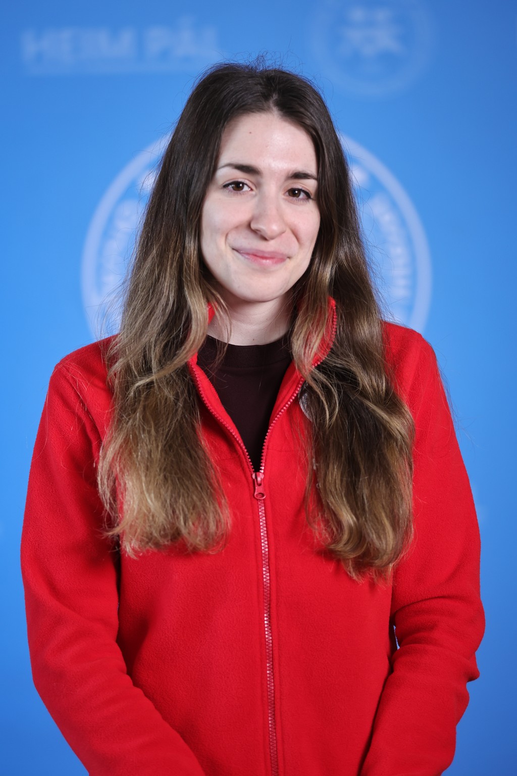 Hosszú barnahajú mosolygós nő piros kardigánban