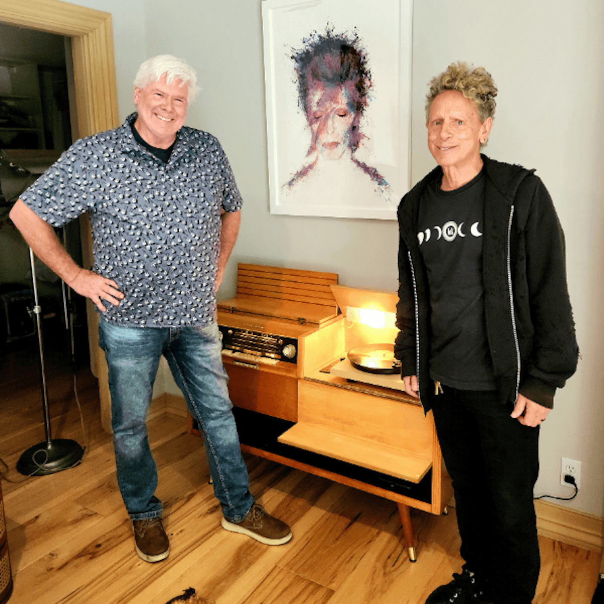 Two men stand beside a restored mid-century stereo console with turntable in a modern showroom.