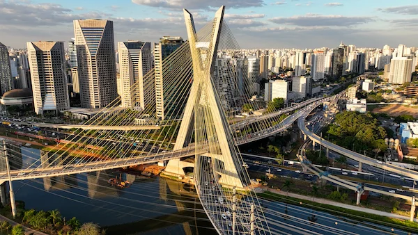 A stylish individual with a green cap and orange glasses holds a coupe glass of green matcha, showcasing unique tattoos and a cozy vibe.