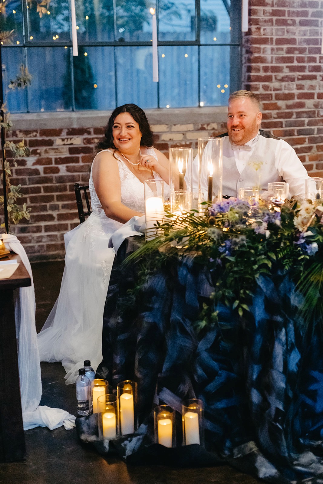 Wedding guests raising glasses in a toast beneath hanging candlelight fixtures.