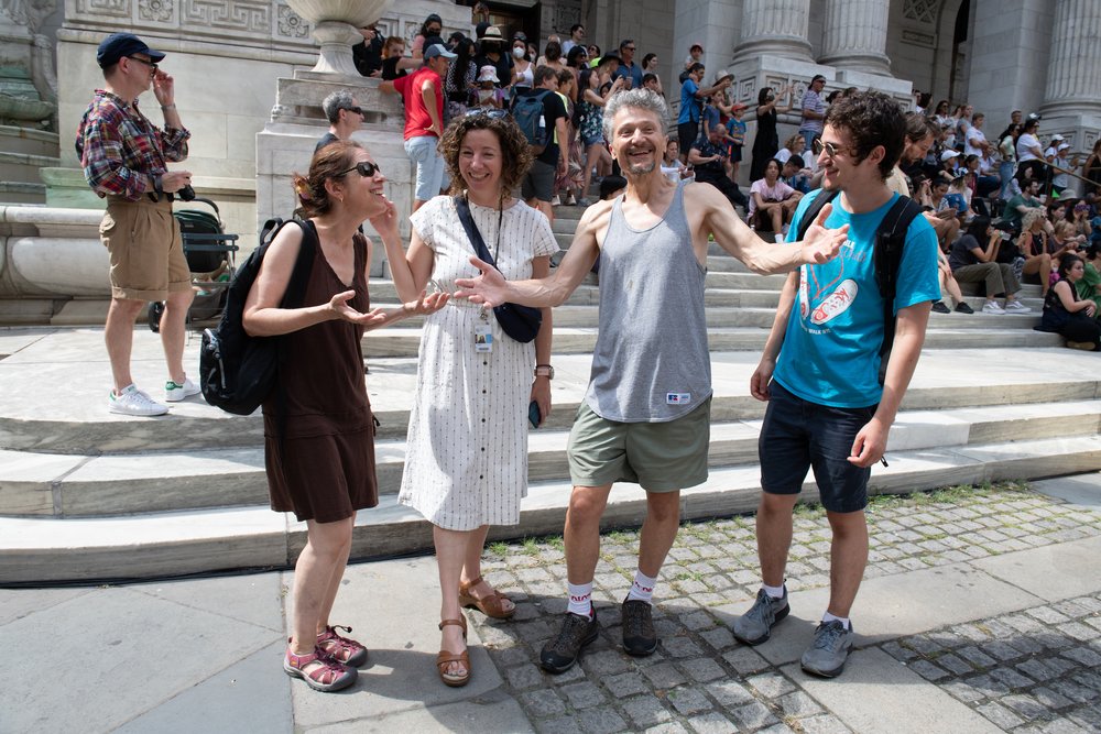 Group of 4 people stand on a sidewalk smiling.