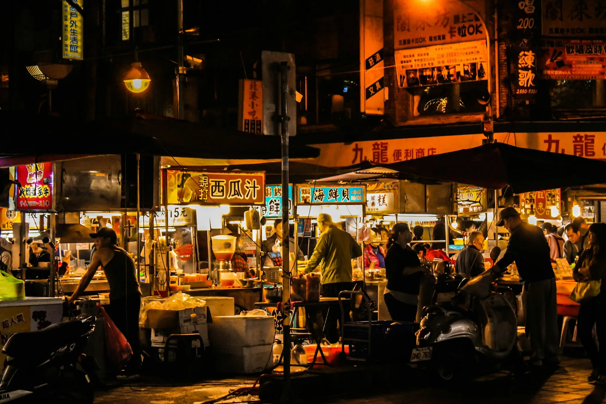 A busy night market lane lined with lit food stalls and people eating