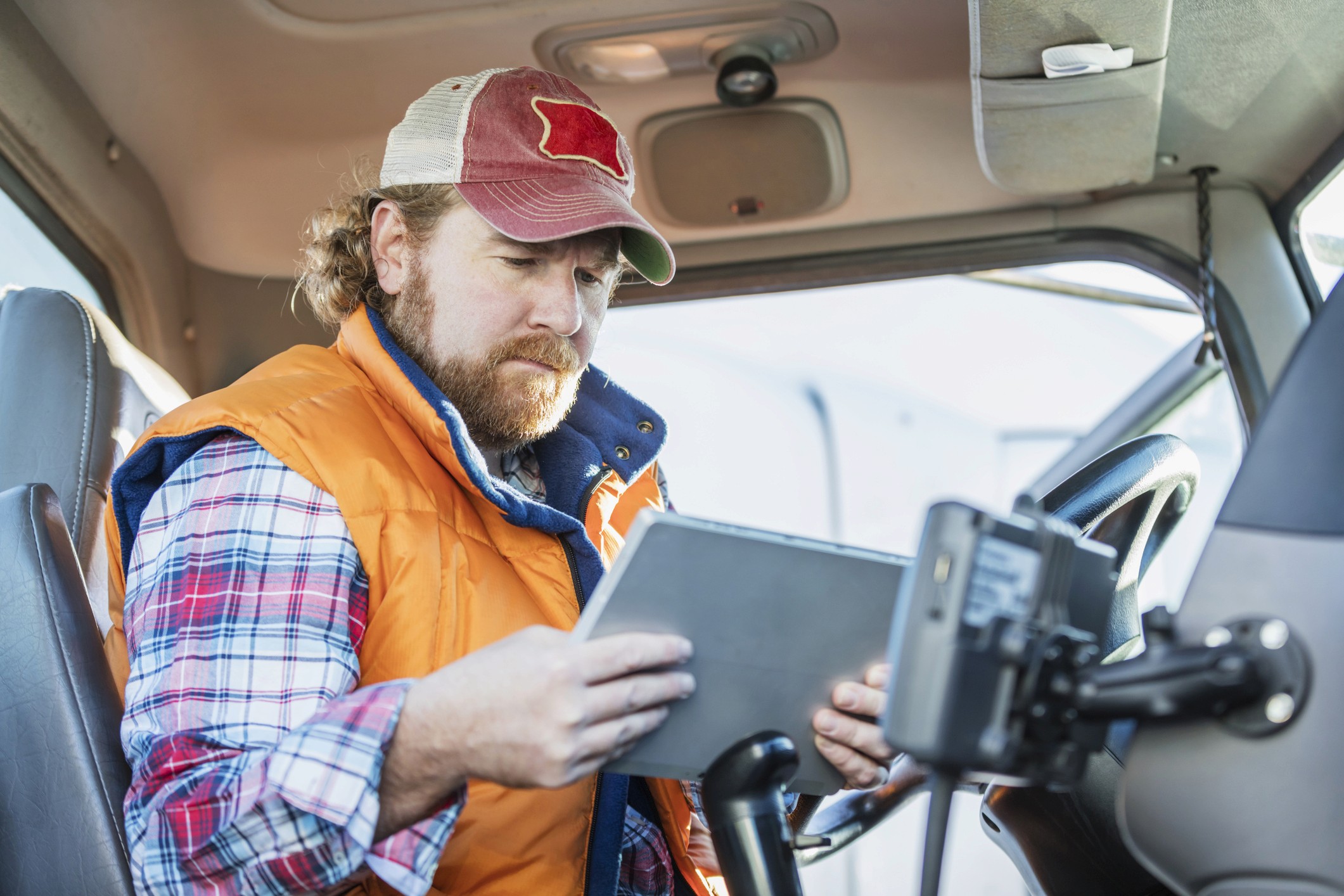 Truck driver in a high-visibility vest using a tablet in the cab to check in before reaching the dock