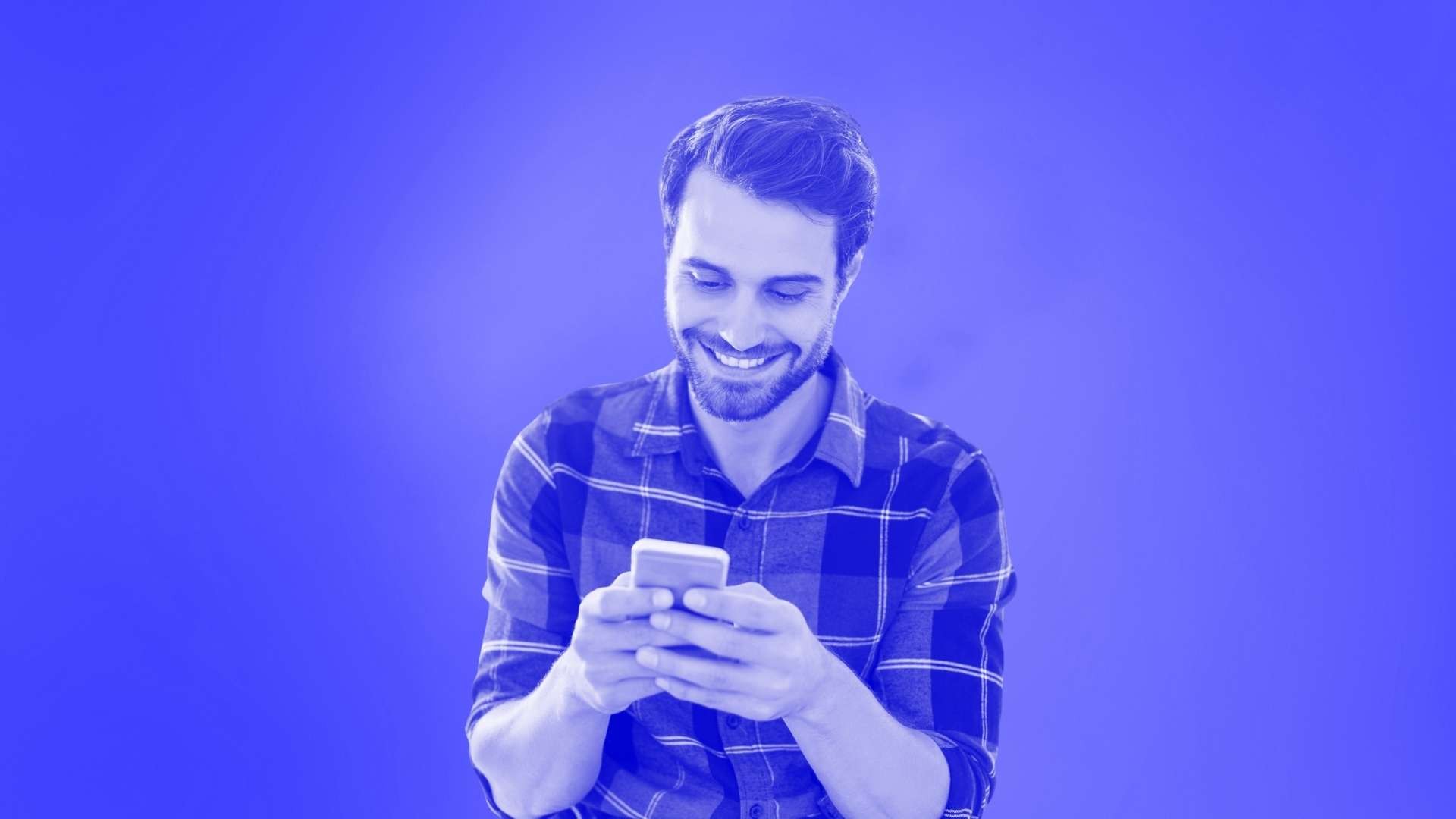 A smiling man in a tartan shirt holding his smartphone in front of him