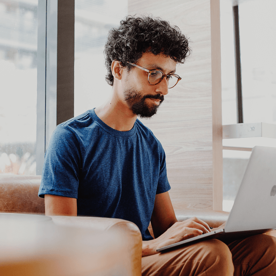 Rodrigo Leles, a digital designer, seated on a chair and working with a laptop in a coffeeshop