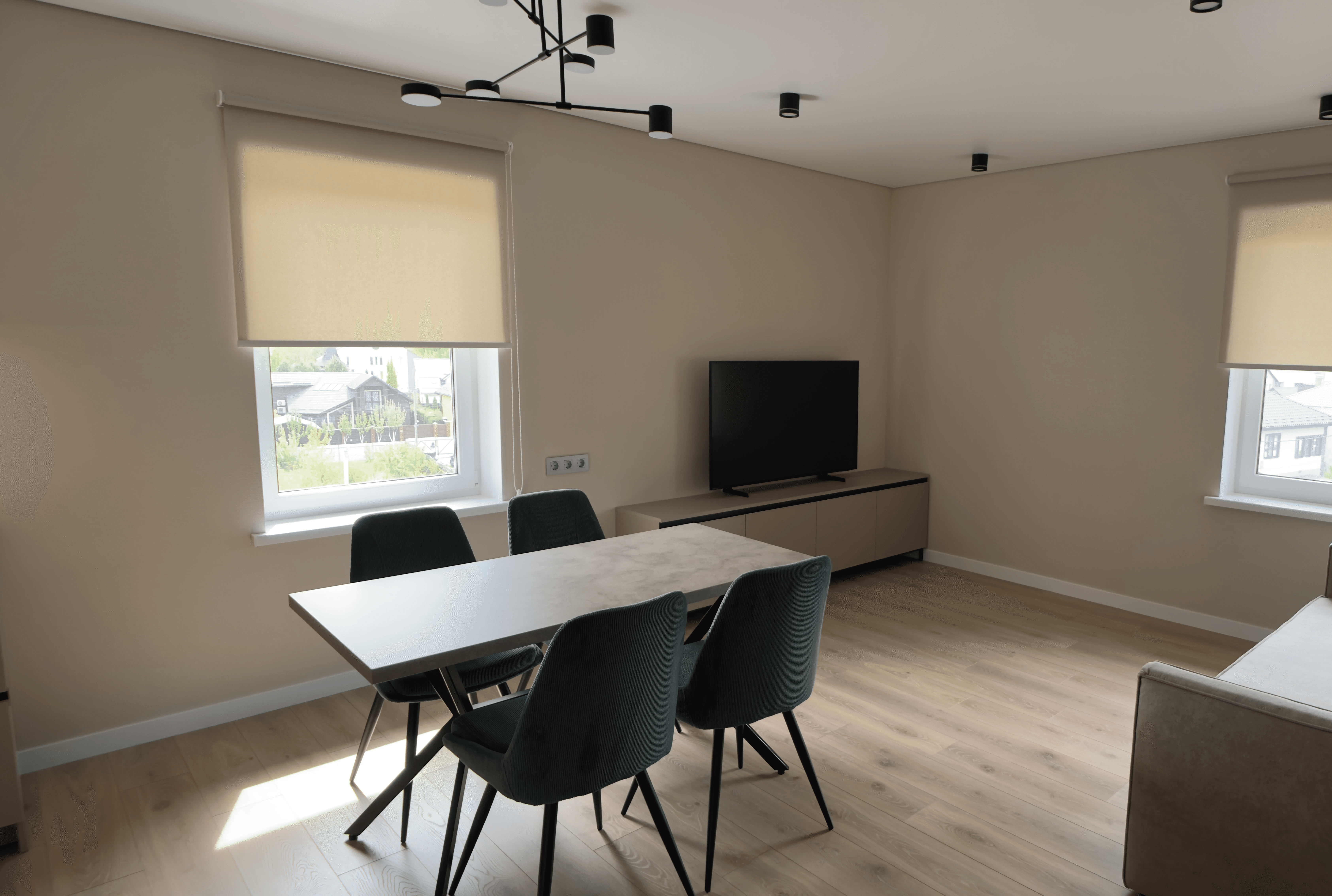 Кутова зона вітальні з телевізором, двома вікнами та обіднім столом