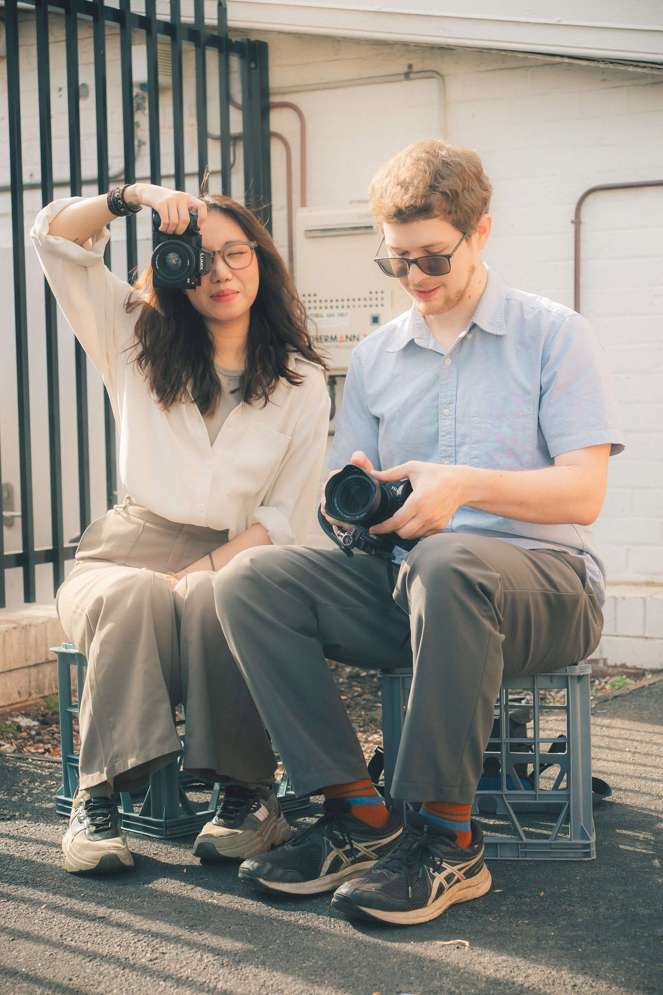 Warm, candid, and dreamy photo of Talia and Liam sitting together; Liam looks down at his camera while Talia holds it up playfully, capturing their creative and joyful spirit. To Love Studio