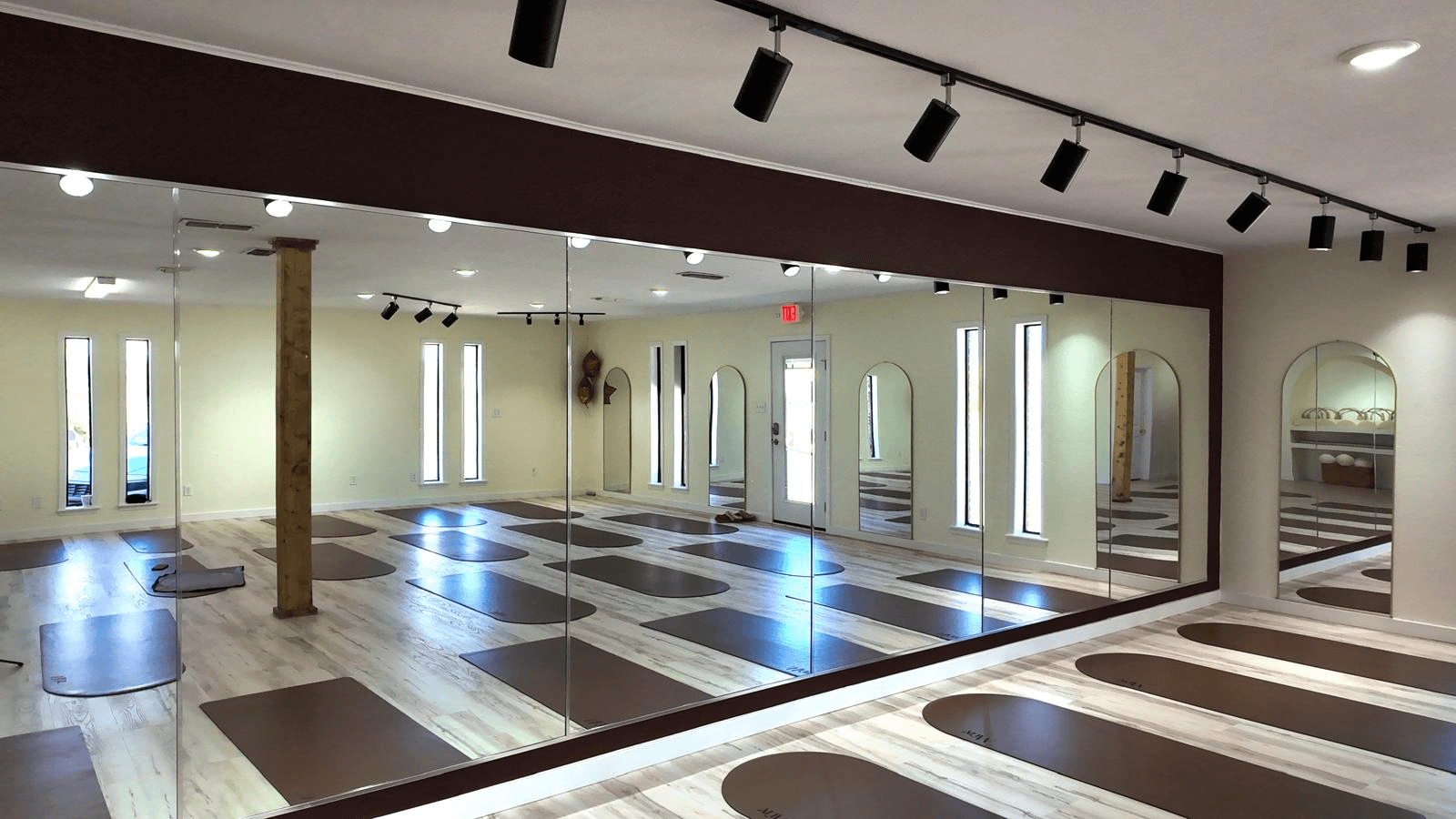 A serene and elegant spa space with wooden reclining chairs and white cushions. Golden sunlight filters through a cascading water feature, creating a peaceful atmosphere. Tropical plants and candles add to the relaxing ambiance.