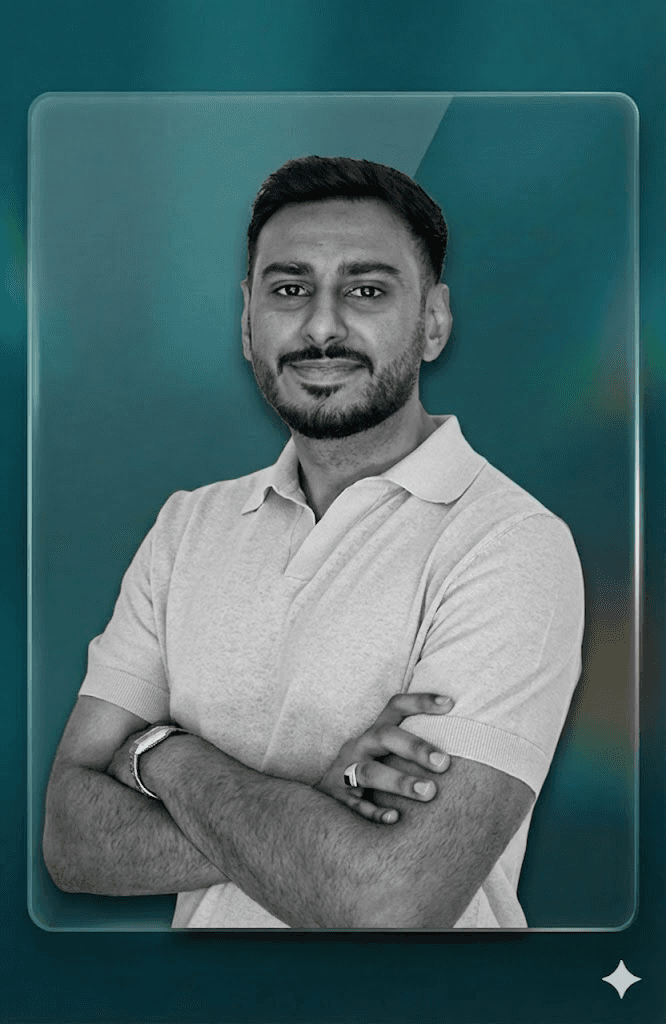 A smiling young man with crossed arms, wearing a plaid shirt and white t-shirt, poses against a dark background.