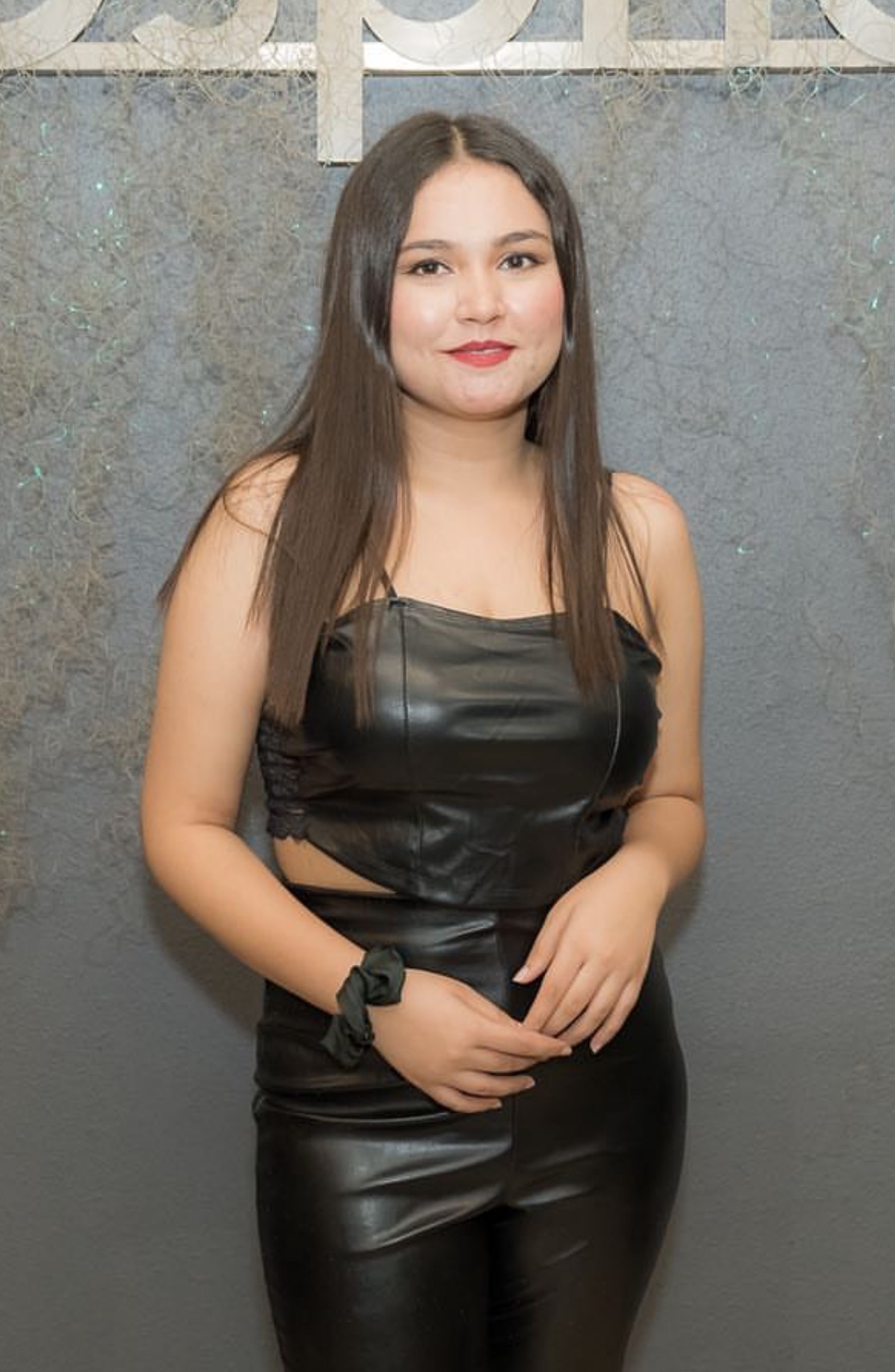 Una persona con una camiseta negra y pantalones de color claro está de pie en la cima rocosa de una montaña al atardecer, sosteniendo una cámara frente a su cara para tomar una foto. Un mar de nubes se extiende detrás de ellos, iluminado por la luz dorada del sol poniente.