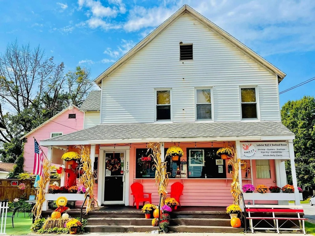 The pink front porch of Eddie F’s on Clinton Street in Saratoga Springs, with red Adirondack chairs, mums and a “Lobster Roll & Seafood House” sign