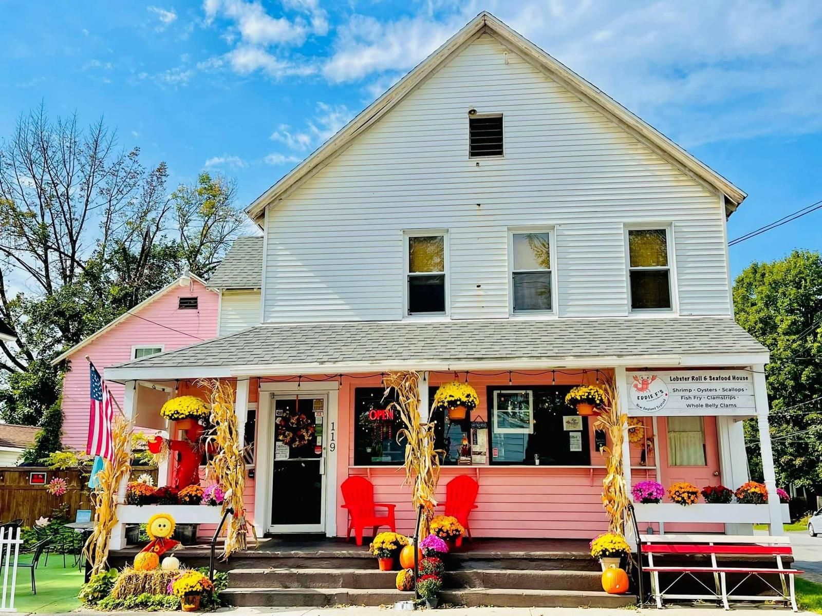 The pink front porch of Eddie F’s on Clinton Street in Saratoga Springs, with red Adirondack chairs, mums and a “Lobster Roll & Seafood House” sign