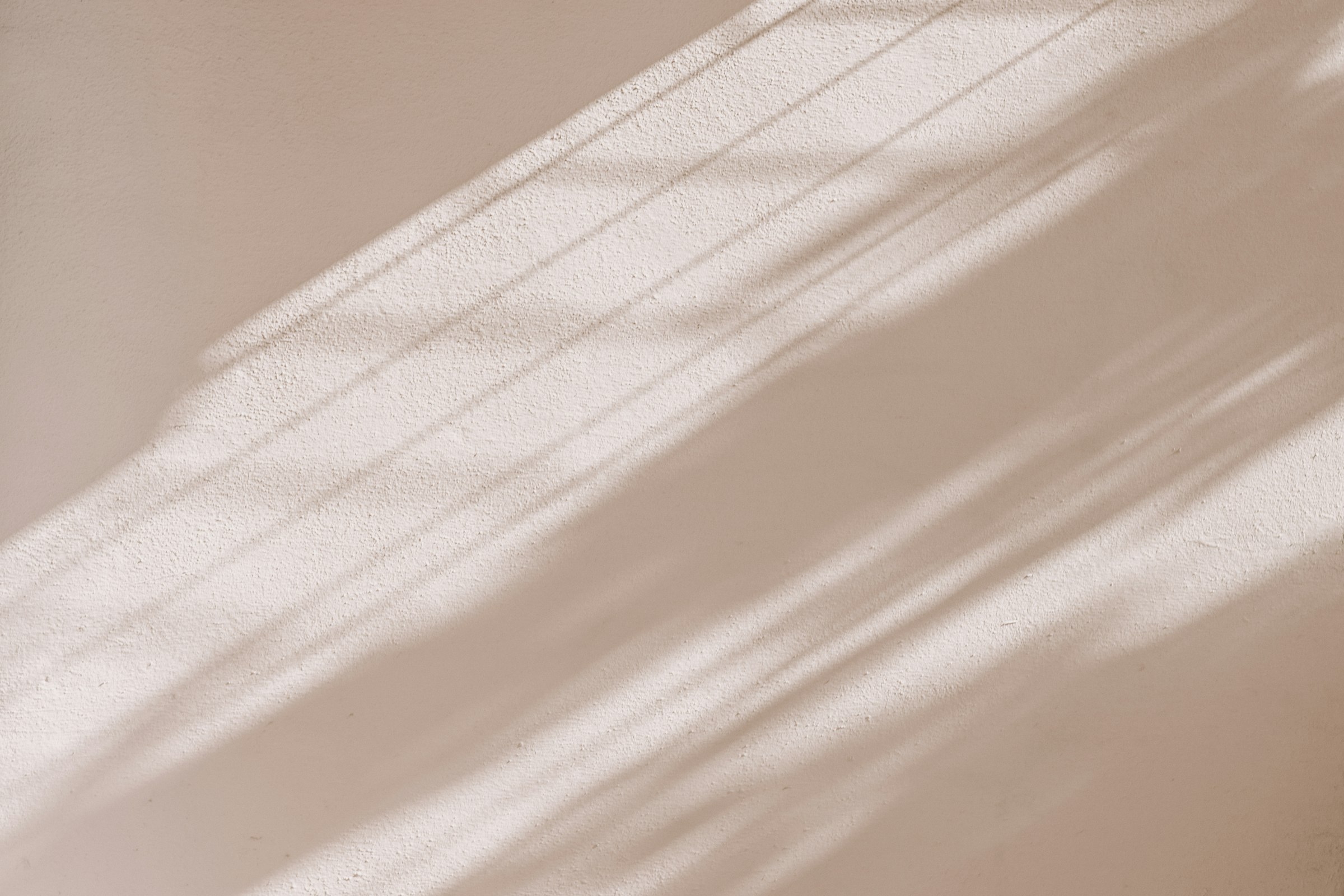 Soft daylight and blind shadows falling across a warm beige wall