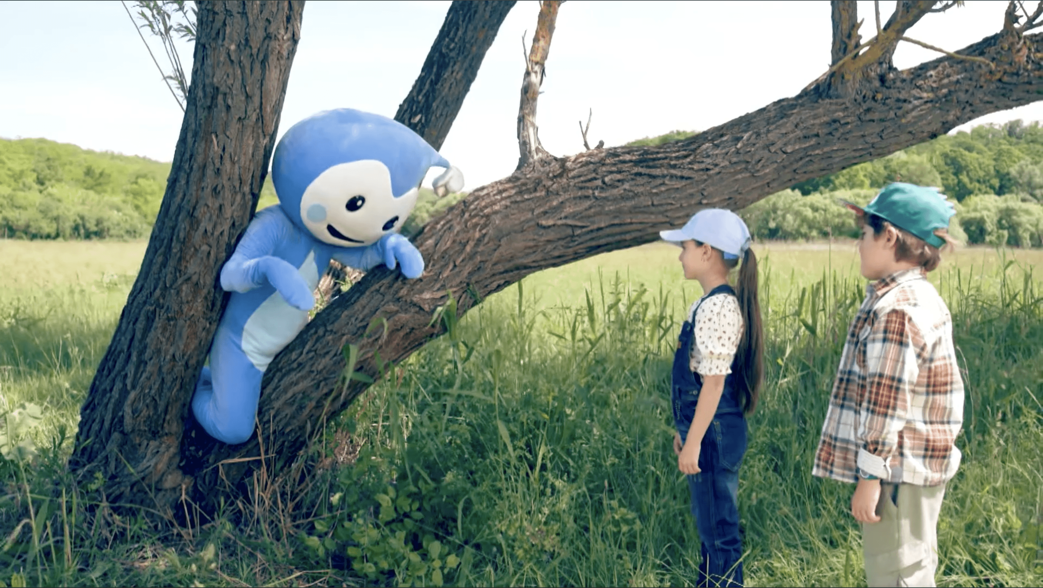 Cseppbarát kék kabalafigurája egy nagy fán ülve tanítja a gyerekeket akik baseballsapkát viselnek.