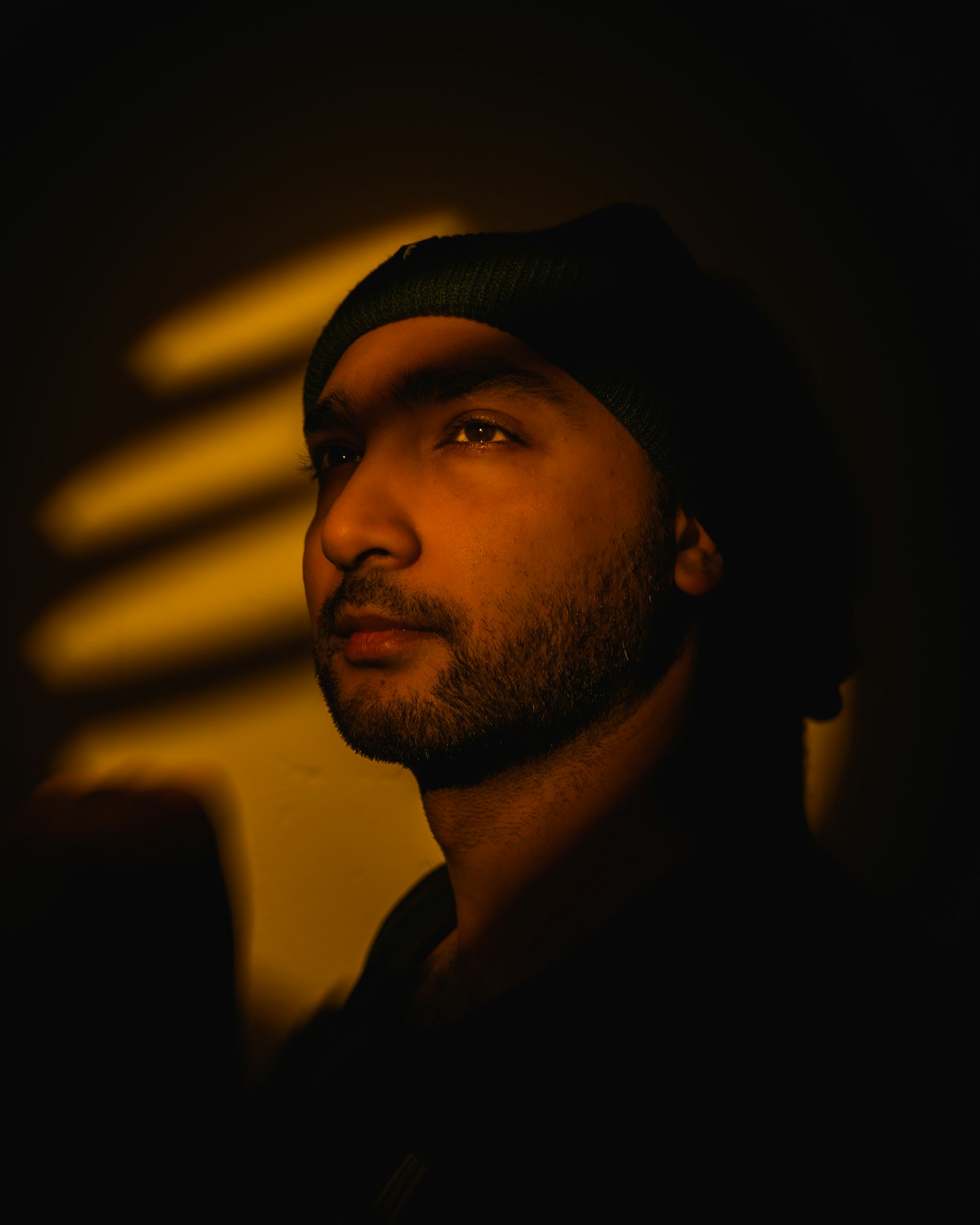 Portrait of a man in a beanie, side-lit by warm striped light