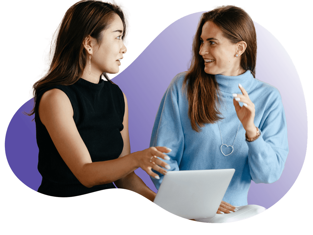 Two women working on laptops at a table, engrossed in their tasks.