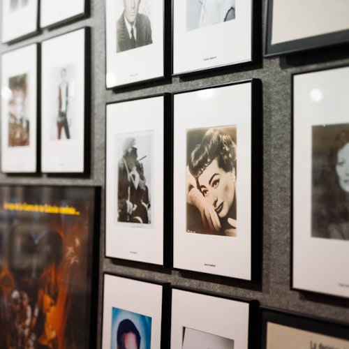 Wall displaying a collage of framed black-and-white and color portraits of various people, arranged closely together.