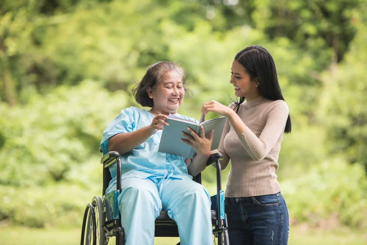 A younger Asian woman spends time caregiving to an older woman in her family who sits in a wheelchair