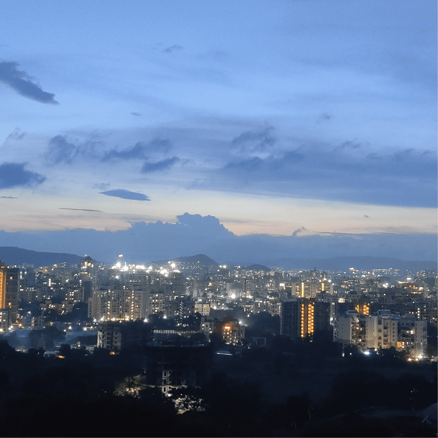 Image of the Pune city skyline at dusk with illuminated buildings and a cloudy sky.