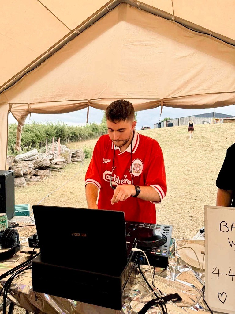 Person wearing a blue puffer jacket and red backpack standing in front of a light blue building on a city street.