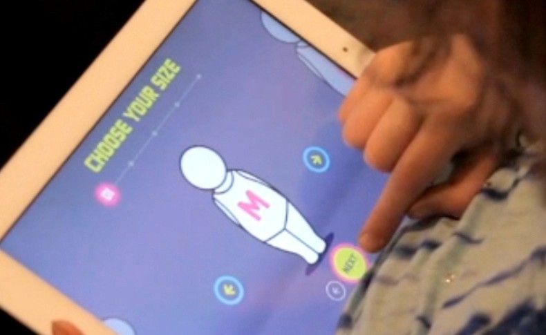 A child's hand points at a colorful, cartoon-style dress on a tablet screen, featuring various patterns, including a cat design, with the text "BABY TO BE REAL" displayed on a purple background.