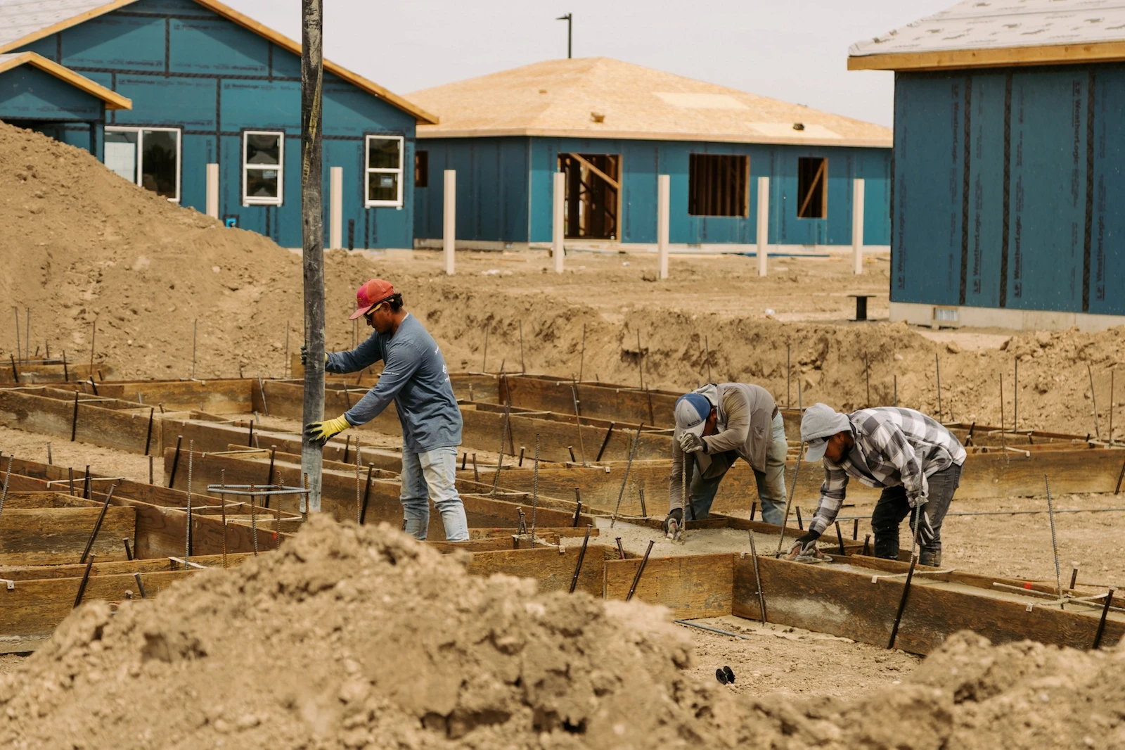 Three construction workers set rebar and prepare concrete forms for a home foundation at a residential building site.