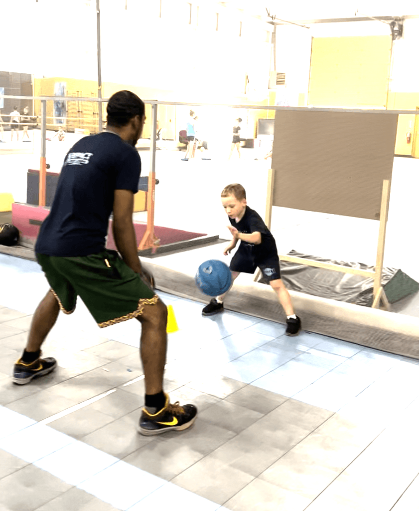 A SportPlus basketball coach helping one student get the correct stance for his dribbling 