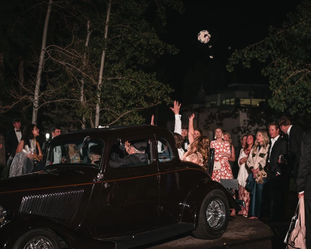 Newlyweds departing in a vintage car as guests wave