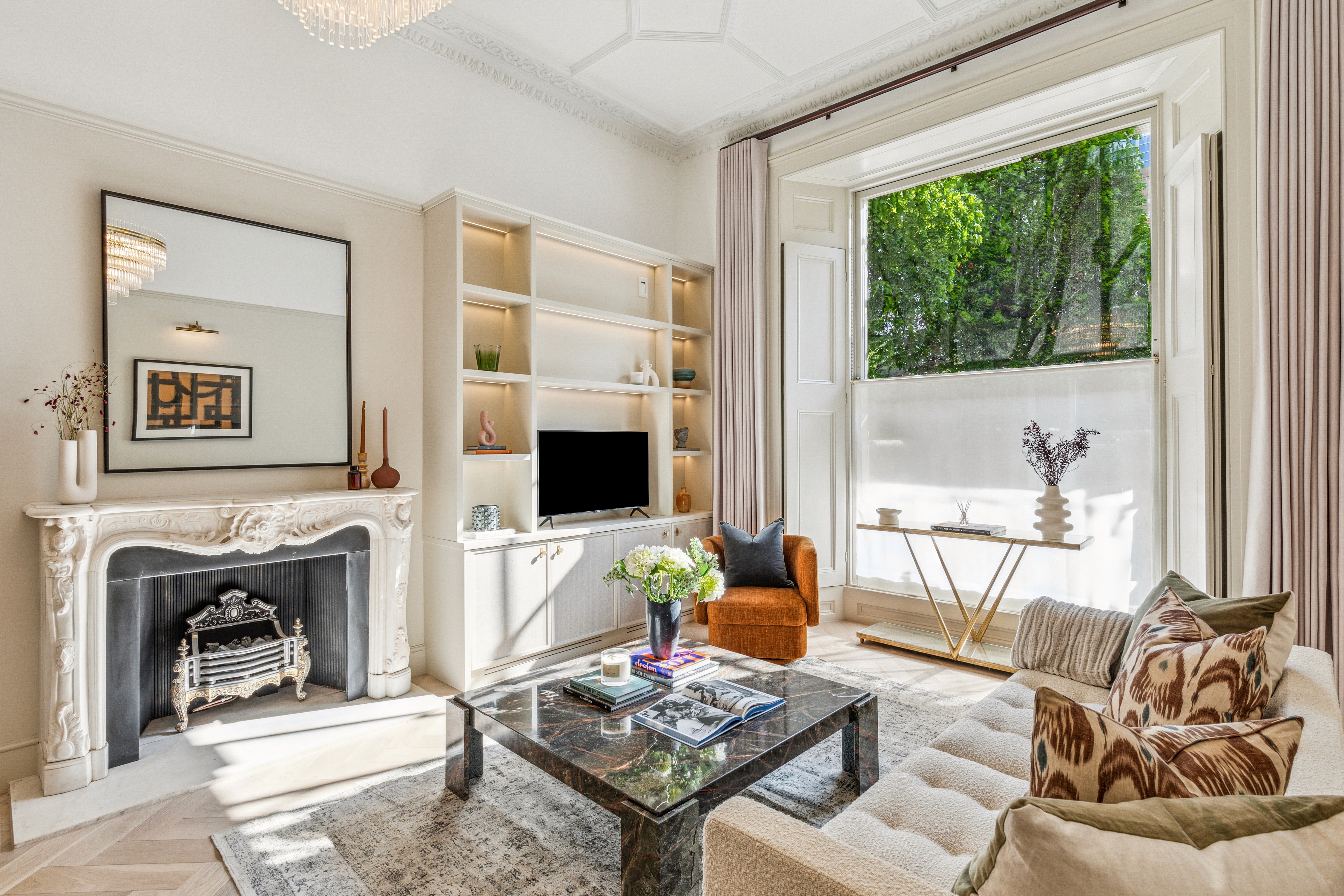 Bright, styled living room with a period fireplace, built-in shelving, large bay window, neutral sofa and a marble coffee table in natural daylight