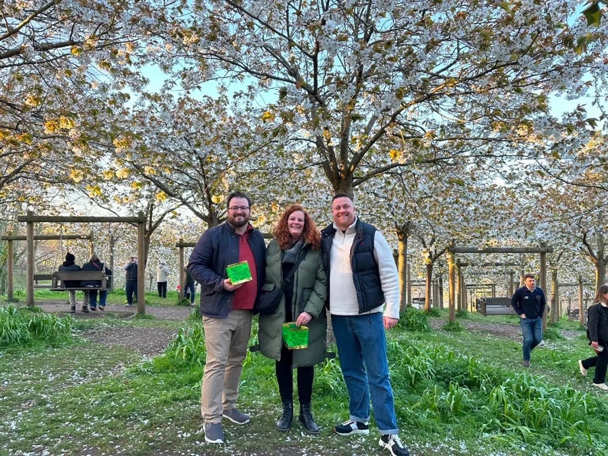 Three people stand in front of cherry blossom trees at Alnwick Garden.