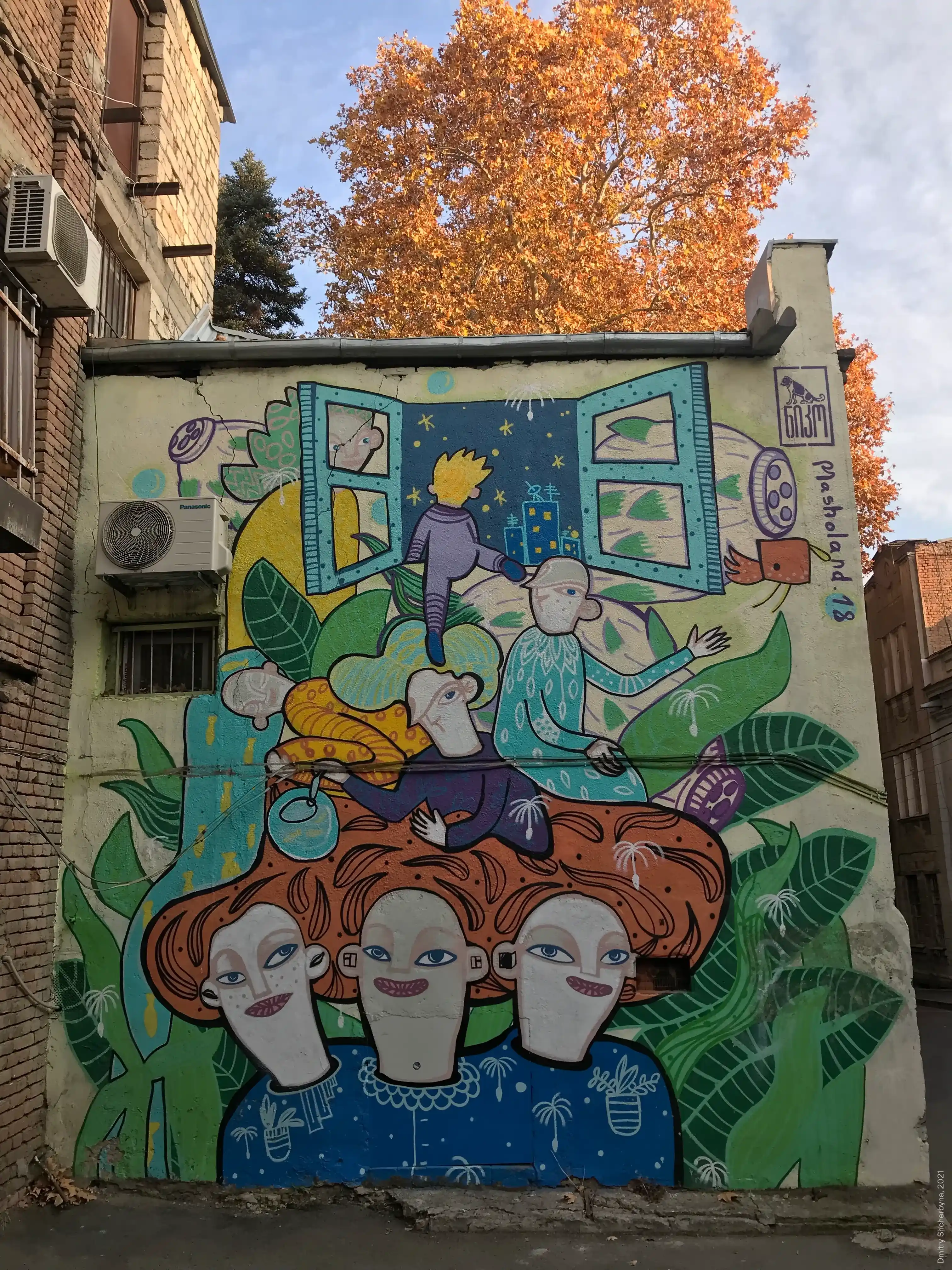A whimsical mural on a small building shows three red-haired people at the bottom, gazing upward. Above them, playful figures are climbing and tumbling through lush green leaves. At the top of the mural, an open turquoise window reveals a starry night sky and a glowing city below.